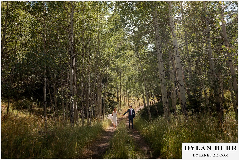antler basin ranch wedding bride and groom holding hands in sunlight on mountain road in aspen trees