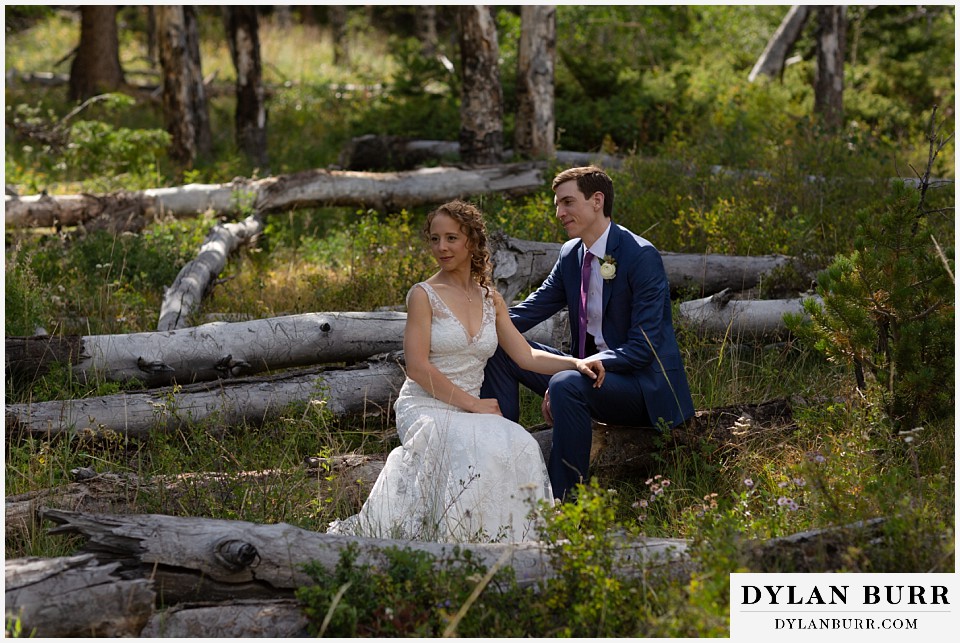bride and groom in forest sitting on fallen trees at antler basin ranch wedding