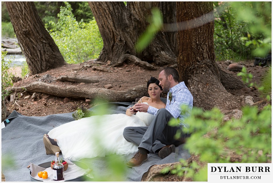 aspen wedding elopement bride and groom toasting while sitting along river