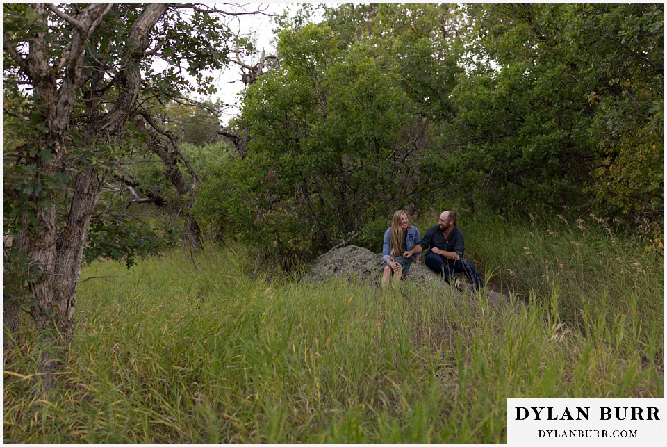 castlewood canyon engagement photos couple sitting on rock along trail laughing