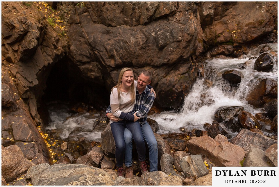 engagement photos in colorado couple on rock with waterfall going into a rock behind them
