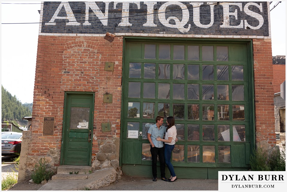 colorado mountain engagement photos colorado wedding photographer dylan burr couple standing by large glass door old antique shop.