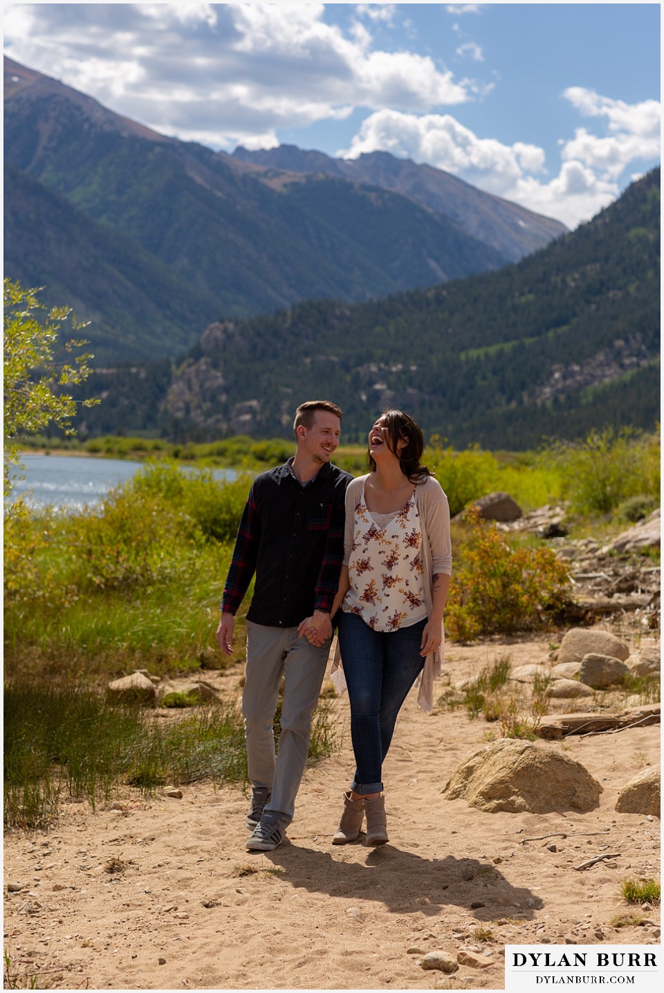 colorado mountain enagagement photos couple holding hands near lake and she is laughing