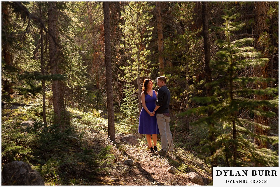 colorado mountain enagagement photos couple standing together in the light cutting through the pine trees