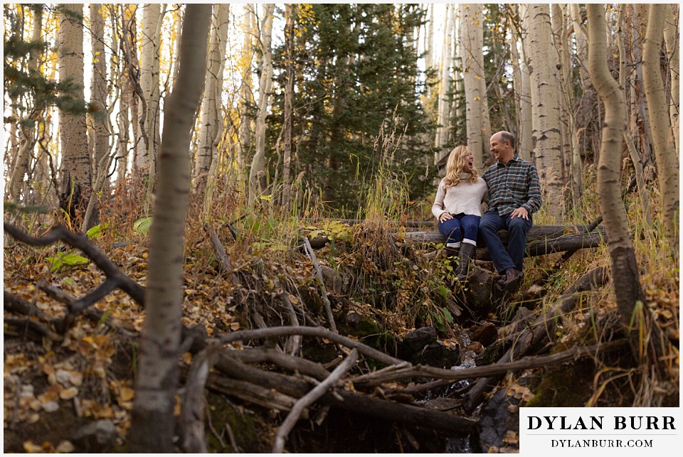 colorado engagement session in mountains sitting near creek laughing
