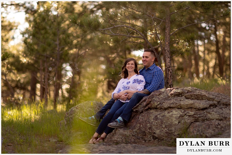 golden colorado mountain enagagement photo session couple taking a minute in forest to sit and relax on a rock