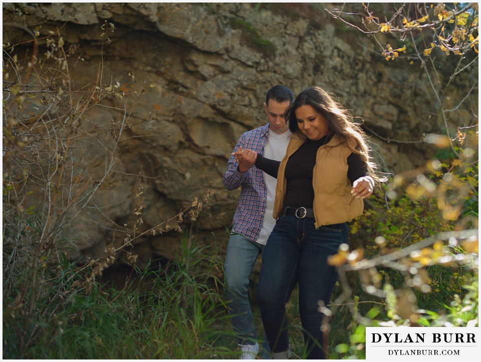 downtown estes park engagement photos walking together near rock wall in the sunlight