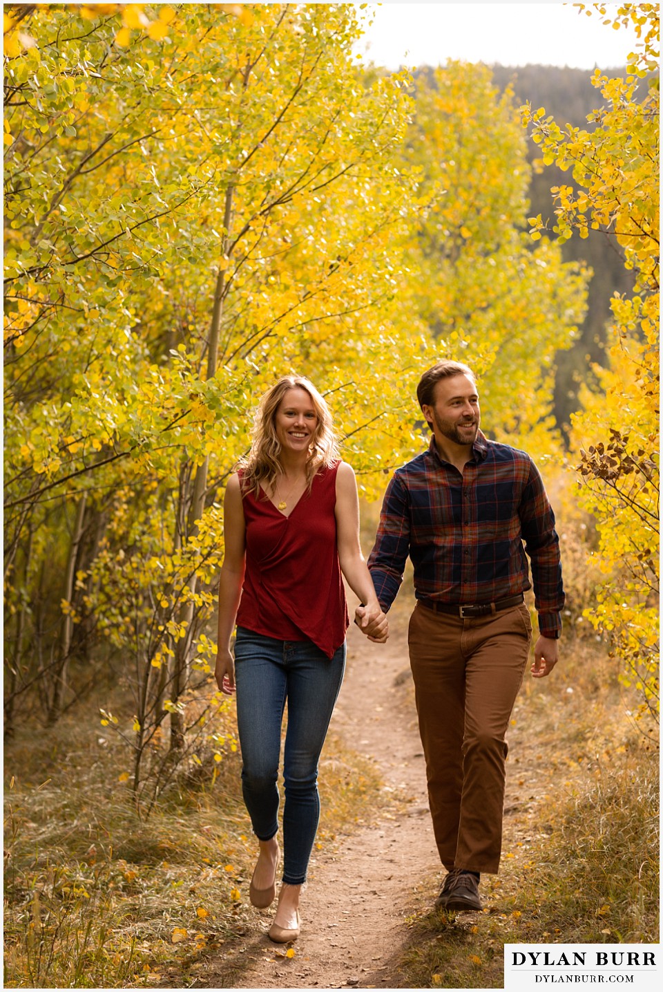 fall engagement photos in colorado couple holding hands walking down trail