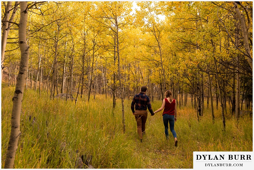 fall engagement photos in colorado couple walking into aspen tree forest