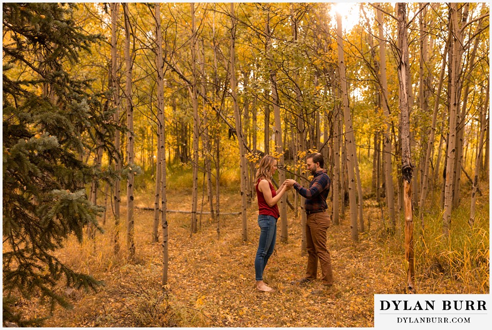 fall engagement photos in colorado couple trying to make whistles with aspen tree leaves