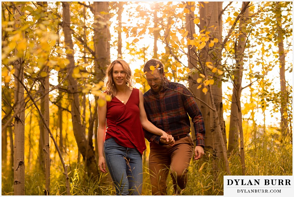 fall engagement photos in colorado couple walking in forest with light peeking through leaves