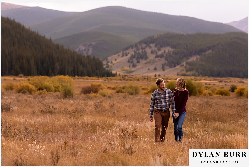 fall engagement photos in colorado couple walking across meadow