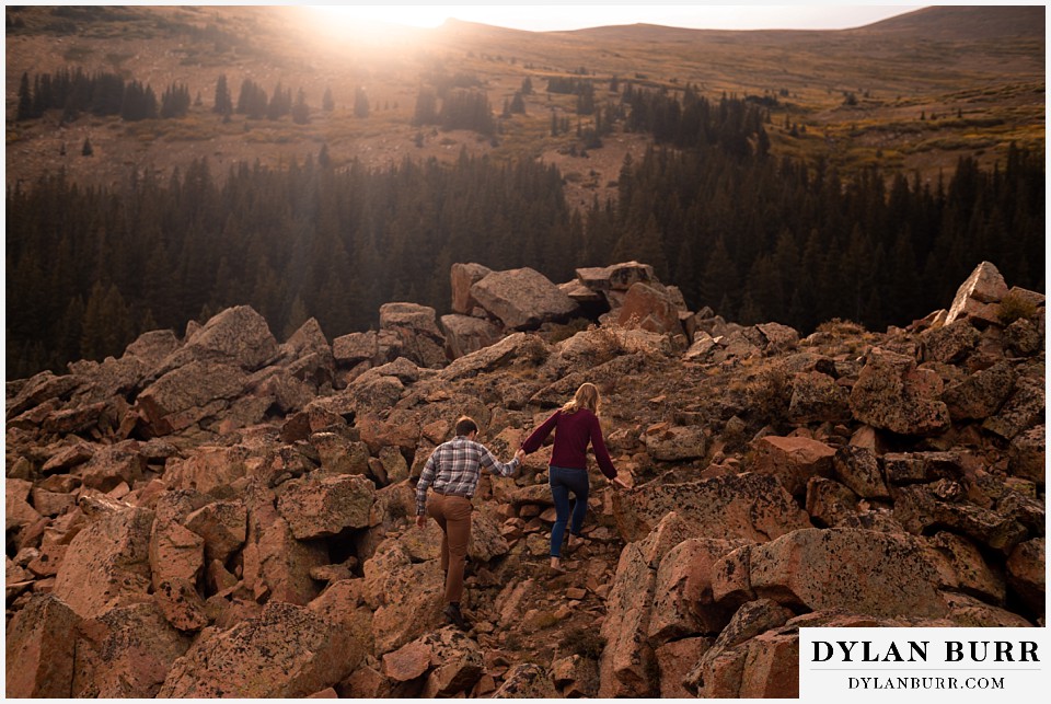 fall engagement photos in colorado couple holding hands hiking on rocks in sun light
