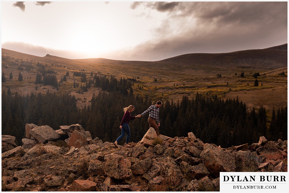 fall engagement photos in colorado couple walking across ridge of boulders