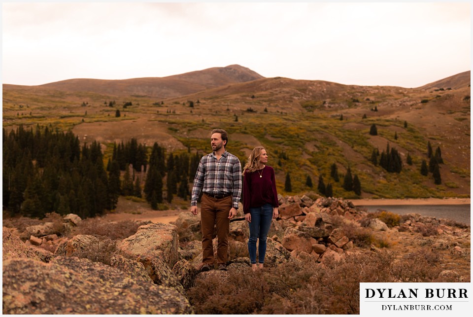 fall engagement photos in colorado couple standing on mountain top together looking out over mountain pass