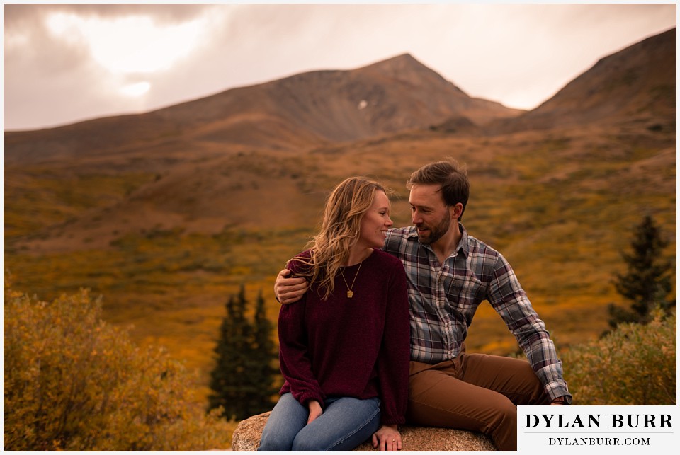 fall engagement photos in colorado couple looking at each other with mountain peaks in background