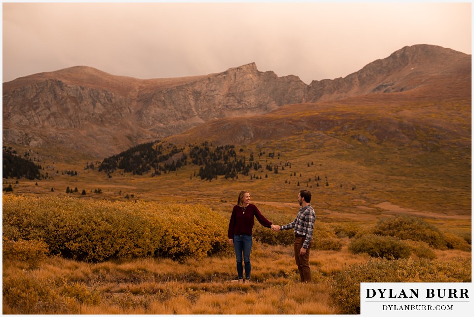 fall engagement photos in colorado standing together in mountain meadow