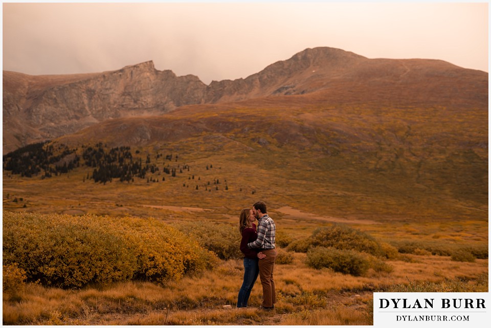 fall engagement photos in colorado couple kissing with huge mountain peaks