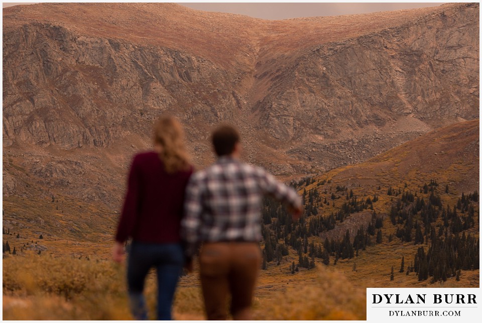 fall engagement photos in colorado mountains in background with couple running in foreground