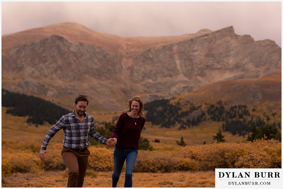 fall engagement photos in colorado couple running together high in mountains