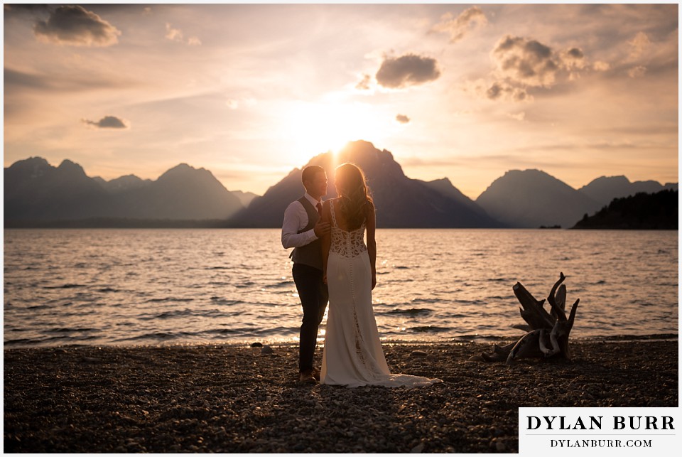 jackson lake lodge wedding grand tetons wyoming bride and groom at jackson lake at sunset with mountains in the background