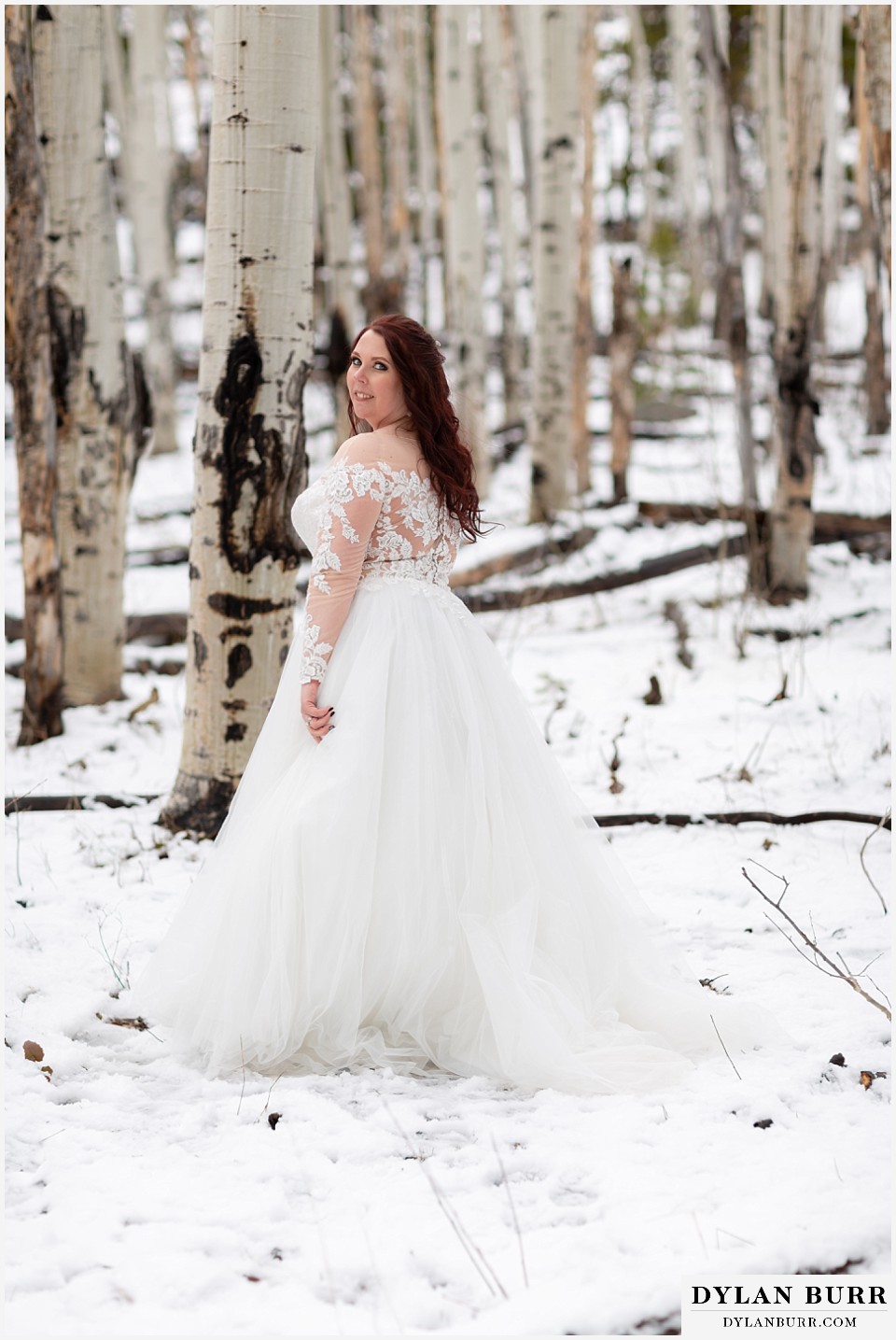 bride standing in snow looks to her husband