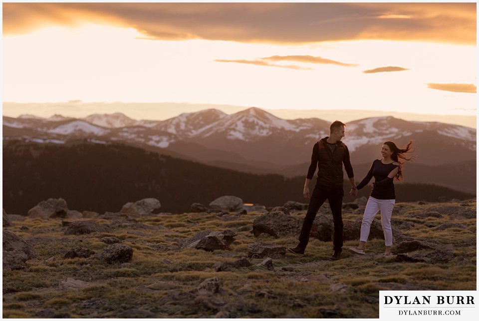 rocky mountain engagement session in colorado couple walking together with hair blowing in the wind on top of a mountain
