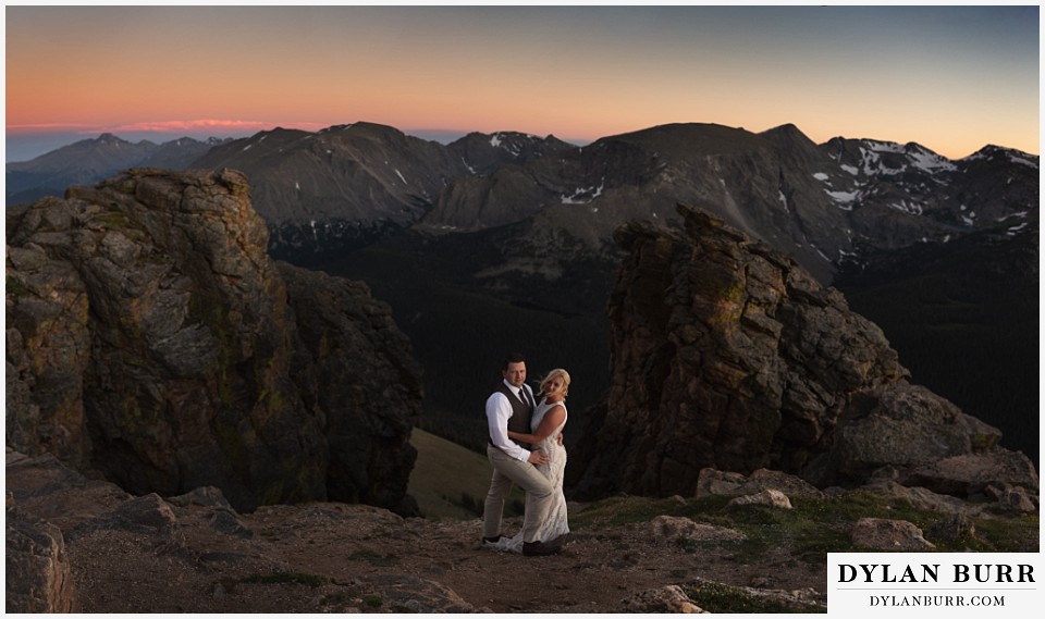 rocky mountain national park wedding elopement bride and groom look on within some mountain rocks and massive mountain range with snow behind them