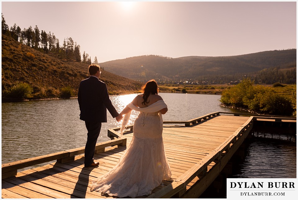 bride and groom walking along lake at sunrise